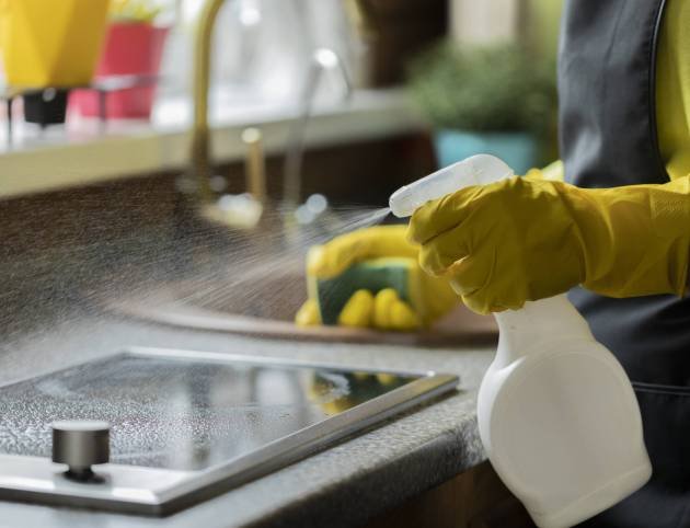 Close up person in yellow rubber gloves cleaning house, wipes kitchen worktop using spray detergent, washes induction stove with sponge. Housework cleaning service, household chores, copy text space